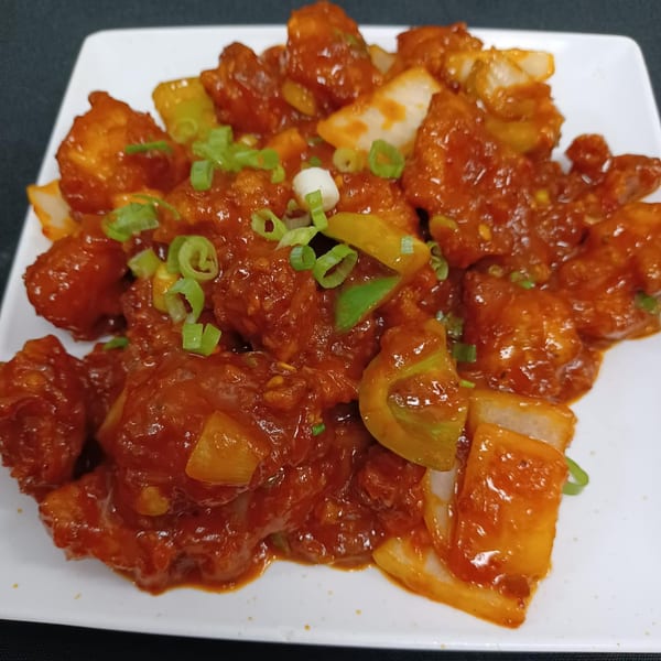 Indian chili chicken, a vibrant dish with red sauce, green onions, and bell peppers on a white plate.