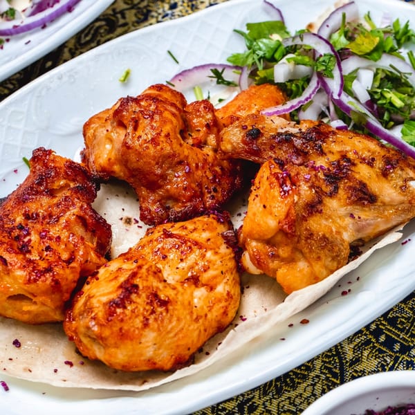 Grilled chicken pieces with red onions and cilantro on a white plate at Biryani Pot Chandler.