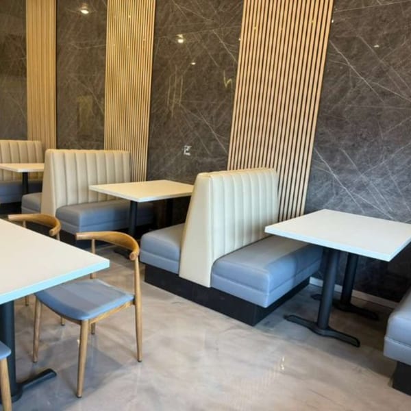 Modern Indian restaurant interior with grey marble walls, light wood panels, and cream and blue booth seating.