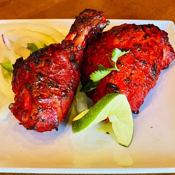 Two pieces of bright red tandoori chicken, garnished with lime wedges and cilantro, on a white plate.