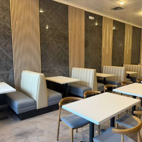 Modern Indian restaurant interior with light-colored booths, white tables, and dark marble walls with wood accents.